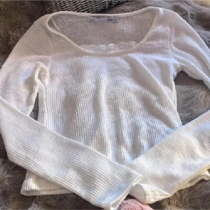 Vit ribbad långärmad topp XS 157 - Superfin vit långärmad topp från 157 i storlek XS. Ribbad och tunn stickad kvalitet med bred rundad halsringning och söt spetsdetalj framtill. Perfekt för dig som gillar en enkel men ändå gullig stil. Sitter snyggt och är lätt att matcha med allt.