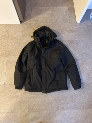 Svart vinterjacka från Beluomo - Svart vinterjacka från Beluomo i storlek M. Jackan har huva med snörning, flera fickor med dragkedja och en quiltad design som håller dig varm. Perfekt för kalla dagar och har en clean, stilren look som funkar till det mesta. Italienskt märke. Skick 8/10. Köptes för 2100kr.