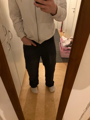 Svarta jeansbyxor med rak passform - Säljer ett par svarta jeansbyxor med klassisk rak passform. Byxorna har normal midja, bälteshällor och dragkedja med knapp framtill. Materialet är jeans och färgen är helsvart, vilket gör dem enkla att matcha med olika stilar.