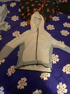 Ljusblå vindjacka från Nike - Säljer en ljusblå vindjacka från Nike med huva och hel dragkedja framtill. Jackan har svarta detaljer längs dragkedjan och nederkanten samt en vit Nike-logga på bröstet. Perfekt för dig som vill ha en sportig och clean look. Storleken är L men passar M också.