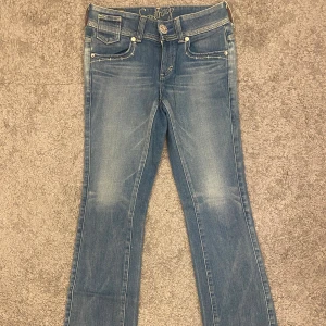 Blå bootcut jeans från Something - Snygga ljusblå bootcut jeans från Something med klassisk femficksdesign och broderade bakfickor med knappar. Jeansen har normal passform och är tillverkade i mjukt denimtyg. Perfekta för en avslappnad och trendig look. Midja rakt över: 36cm Lår: 23cm Innerben: 73cm