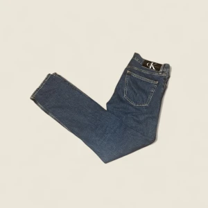 Blå jeans från Calvin Klein - Klassiska blå jeans från Calvin Klein med rak passform och snyggt CK-märke på bakfickan. Jeansen har fem fickor och är tillverkade i slitstarkt denim. Perfekta för en avslappnad och stilren look. Original pris:1299.  Mitt pris:299