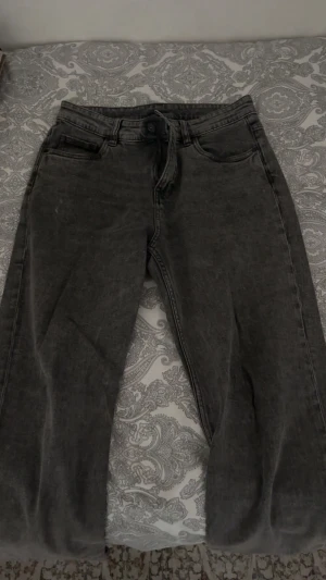 Mörkgrå jeans från Kappahl, strl 164 - Snygga mörkgrå jeans från Kappahl i storlek 164. Klassisk femficksmodell med raka ben och normal passform. Jeansen har en cool tvättad look och är tillverkade i mjukt denimtyg med dragkedja och knapp framtill.
