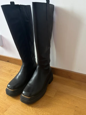 Svarta höga boots från Steve Madden - Säljer ett par svarta höga boots från Steve Madden. Boots i skinn med dragkedja på insidan och cool metall-detalj framtill på sulan. Utgångspris 2399kr. Använda en gång!