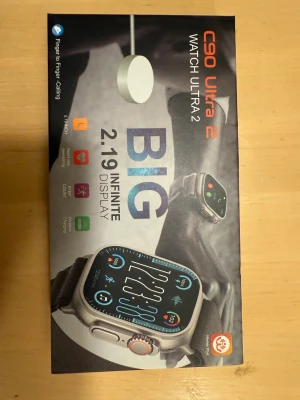 C90 Ultra 2 smartwatch med stor display - C90 Ultra 2 smartwatch med 2,19-tums stor display, svart sportarmband och metallisk boett. Klockan har funktioner som pulsmätning, stegräknare och trådlös laddning. Modern design med fyrkantig form och tydliga knappar på sidan. Perfekt för dig som gillar teknik och smarta funktioner.