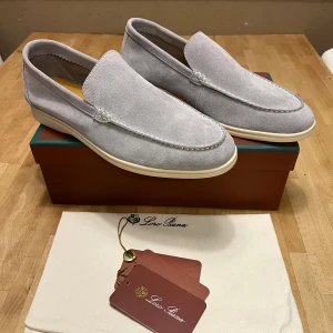 Ljusgrå mockaloafers från Loro Piana - Snygga ljusgrå loafers från Loro Piana i mjuk mocka med vit sula och diskreta sömmar. Klassisk och stilren design med rund tå och platt sula, perfekta för en clean och avslappnad look. Kommer med originalbox och dustbag.