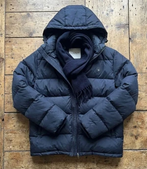 GANT | Active Cloud | Mörkblå - Säljer en mörkblå pufferjacka från Gant med huva och dragkedja. Jackan har en clean look med diskret logga på bröstet och breda, quiltade paneler. Perfekt för kalla dagar och riktigt skön att bära. Klassisk passform och stilren design. Säljer den för 600kr billigare, använd kanske en vecka och märkte att den inte passa min klädd stil. Bilder och sådant är bara att fråga om, pris går att diskutera om det är en snabb affär.