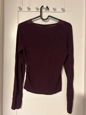 Vinröd långärmad topp med spets - Säljer en vinröd långärmad topp med snygg v-ringning och spetsdetaljer vid halsen. Toppen har en slim passform och är tillverkad i mjukt bomullsmaterial. Perfekt för dig som gillar stilrena plagg med en liten twist.