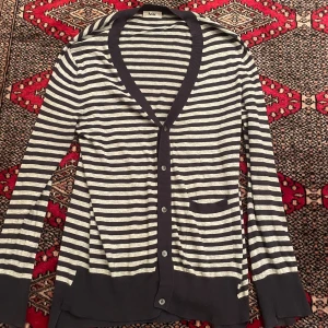 Kaschmir kofta från Acne i svart grå - Säljer en snygg archive randig kofta från Acne i svart och grått. Acne studios. Koftan har v-ringning, knappar hela vägen och en liten ficka framtill. Perfekt att slänga över en t-shirt för en chill look. Är cachmire bladning och väldigt mysigt material