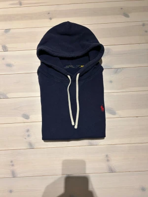Ralph Lauren - Snygg mörkblå hoodie från Polo Ralph Lauren med klassisk röd logobrodyr på bröstet. Använd fast i bra skick | inga fläckar eller hål | lite nopprig men inget som syns på håll | nypris 2000+ | perfekt som julklapp | pris går att diskutera vid snabb och enkel affär✅