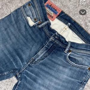 Blå jeans från Acne Studios - Snygga blå jeans från Acne Studios med klassisk femficksdesign och ljus tvätt. Jeansen har raka ben och normal passform, med detaljer som metallknappar och bälteshällor. Perfekta för dig som gillar stilrena och tidlösa jeans.