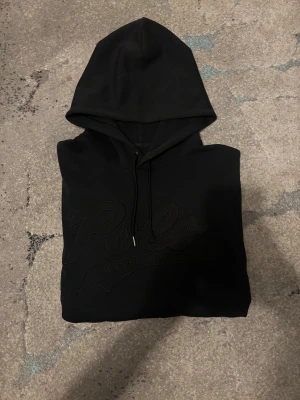 Svart hoodie från Polo Ralph Lauren - Svart hoodie från Polo Ralph Lauren med stor broderad logga framtill. Klassisk modell med huva och dragsko, tillverkad i mjuk bomullsblandning. Perfekt för en chill och stilren look.