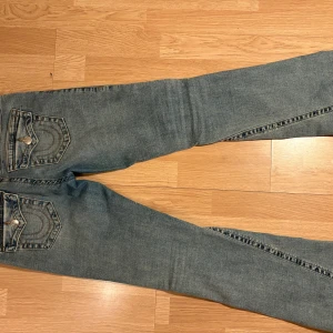 True Religion Joey Low Rise Flare Jeans - Säljer ett par blå True Religion Joey jeans med låg midja,  Tillverkade i slitstarkt denim Säljer ett par jeans från true religion storlek 27 i en dassig blå fin färg. Säljer ett par jeans från true religion storlek 27 i en dassig blå fin färg. Använda ett par gånger bara då de e lite för stora för mig! Köpta i slutet på juni detta år för cirka 1300-1400 i jättebra skick💕   Mått: Innerbenslängd: 79cm  Midjemått: 40cm rakt över o så x2 för att få måttet runt hela.  Höftmått: 45cm rakt över och x2