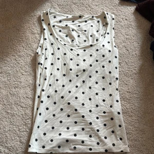 Vit prickig linnetopp från ZARA - Säljer en vit linnetopp från ZARA i storlek S med svarta prickar över hela toppen. Modellen är ärmlös med rundad halsringning och har en slim passform. Materialet är mjukt och stretchigt, troligen bomull eller syntet. Perfekt för dig som gillar lekfulla mönster!
