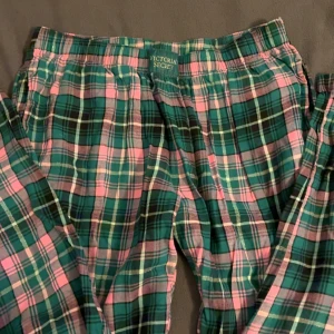 Rutig pyjamasbyxa från Victoria's Secret - Mysiga pyjamasbyxor från Victoria's Secret i grön, rosa och vit rutig bomull. Byxorna har resår i midjan och en avslappnad passform, perfekta för chill hemma. Klassisk rutig design som känns både söt och trendig.