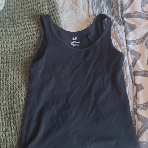 Svart linnetopp från H&M - En klassisk svart linnetopp från H&M i bomull. Toppen är ärmlös med rundad halsringning och har en enkel, stilren design som passar till allt. Perfekt för sommardagar eller som lager under andra plagg.