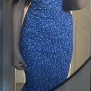 Blå långklänning med prickigt mönster - Säljer en blå långklänning med vitt prickigt mönster. Klänningen har en figurnära passform och är ärmlös, vilket ger en snygg och modern siluett. Perfekt för dig som gillar färg och mönster. Fråga gärna om fler bilder eller mått!