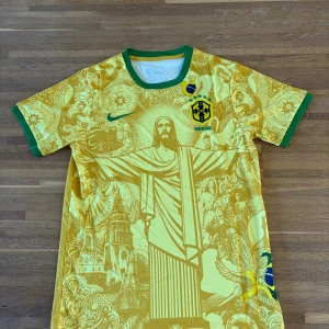 Gul Brasil fotbollströja Nike CBF | Kristusmotiv & unika detaljer - Säljer en gul Brasilien fotbollströja från Nike med gröna detaljer och CBF-emblem på bröstet. Tröjan har ett unika tryck med Kristusstatyn och brasilianska motiv, rund hals och kortärmad modell. Tillverkad i lätt och ventilerande material – perfekt för match, träning eller streetwear.  ✔️ Lätt och andas ✔️ Kortärmad, regular fit ✔️ Aldrig använd  Storlek: M Skick: Ny / aldrig använd 