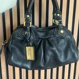 Marc Jacobs väska - svart - Marc Jacobs classic q baby groove med guldiga detaljer. Väskan är svart. Axelremband ingår. Den är ca 30 cm bred och är i den lilla modellen. Mycket bra skick. Finns lite slitningar på axelrembandet och fötterna, se bilder. Lätt missfärgning i väskan. Fler bilder finns och svarar gärna på frågor 🖤