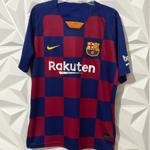 FC Barcelona Messi 10 matchtröja Nike - Säljer en officiell FC Barcelona fotbollströja från Nike med Messi 10 på ryggen. Tröjan har blå och vinröda rutor, klubbmärke på bröstet, Rakuten och Beko-loggor samt gula detaljer. Tillverkad i lätt och ventilerande polyester, perfekt för fotbollsälskare.