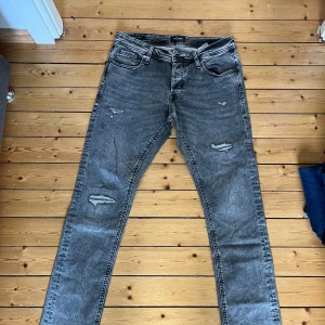 Grå slitna skinny jeans - Säljer ett par grå skinny jeans med slitningar på låren och knäna. Jeansen har klassisk femficksdesign och dragkedjegylf. Perfekta för dig som gillar en lite tuffare stil.