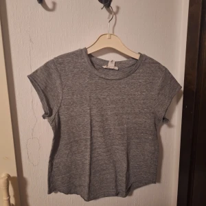 Grå t-shirt - En basic grå t-shirt från Forever 21 i mjuk bomullsmix. Modellen har rund halsringning, korta ärmar med råa kanter och en avslappnad passform. Perfekt att styla med jeans eller kjol för en enkel och clean look.