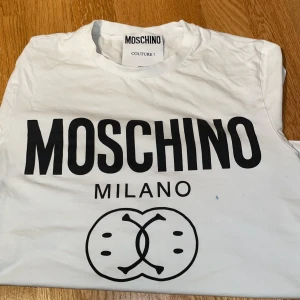 Vit Moschino Milano t shirt - Vit t shirt från Moschino med stor svart logga och Milano tryck framtill. Klassisk rund hals och korta armar. Tillverkad i mjuk bomull för en skön känsla. Perfekt statement plagg för dig som gillar exklusiva märken och stilren design.                Pris kan diskuteras vid snabb affär!