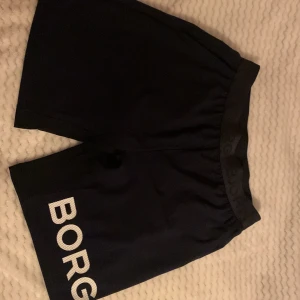 Svarta Björn Borg träningsshorts M - Snygga svarta träningsshorts från Björn Borg i storlek M. Shortsen har elastisk midja och stort vitt BORG-tryck på ena benet. Perfekta för gymmet eller sport, tillverkade i ett lätt och smidigt material som andas.