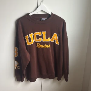 Brun UCLA sweatshirt från H&M Divided - Collegeinspirerad brun sweatshirt från H&M Divided med stor gul och vit UCLA-tryck på bröstet och  tryck på ena ärmen. Oversized fit med rund hals och långa ärmar. Använd 2/3 ggr kanske. 