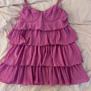 Rosa volangklänning från Zara - Supersöt rosa kortklänning från Zara med tunna axelband och flera lager volanger. Klänningen är plisserad och har en luftig,  säljer pågrund av att den är för kort för mig. Ni kan förslå pris! Rekomederar xs eftersom den är liten på mig som är S