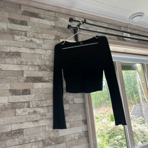 Svart croppad topp med twist framtill - Säljer en svart långärmad topp från Shein med croppad passform och snygg twist-detalj framtill. Toppen har en djupare v-ringning och är tillverkad i mjuk bomullsmix som sitter skönt på kroppen. Perfekt för att lyfta din outfit.