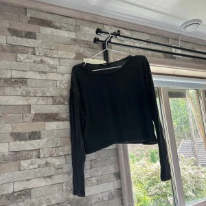 Svart croppad långärmad topp BikBok - En svart croppad långärmad topp från BikBok. Enkel och stilren design med rund halsringning. Perfekt att matcha med höga jeans eller kjol för en chill look.