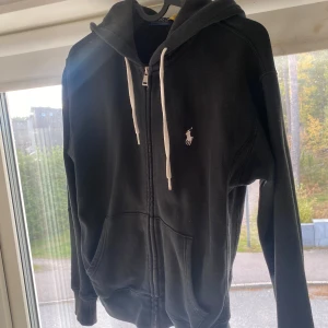Svart hoodie från Ralph Lauren - Svart hoodie från Ralph Lauren med vit broderad logga på bröstet. Skicket är 8/10 Inga defekter eller nånting som är skadat. Strl är xs. Jag är 172 och den passar. Tveka inte på att höra av er. Fraktar efter 1-3 dagar