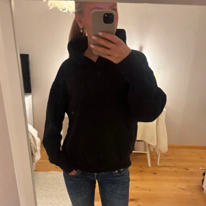 Svart hoodie från Weekday XS - En svart hoodie från Weekday i storlek XS. Klassisk modell med huva och magficka, perfekt för chill dagar. Oversized fit och mjukt material som känns skönt mot huden. Passar dig som gillar en enkel och stilren look.