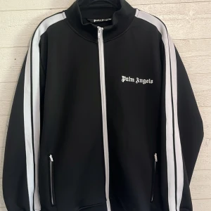 Palm Angels svart track jacket - Säljer min sjukt snygga Palm Angels tröja som är i sjukt bra skick! Jag fick tröjan i present av min bror för ca 1 år sedan och är endast använd ca 3-5 gånger då den inte passar mig! Hör av er vid intresse!