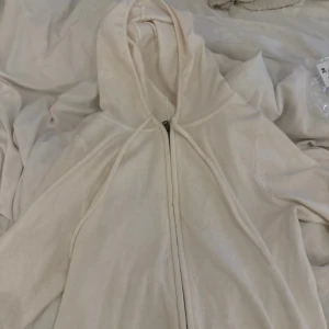 Beige hoodie med dragkedja - Säljer en stilren beige hoodie med dragkedja och huva. Tröjan har långa ärmar med ribbade muddar och är tillverkad i mjukt material, perfekt för en avslappnad look. Enkel och clean design som passar till det mesta.