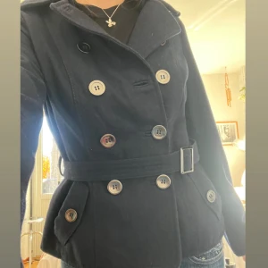 Mörkblå kappa med bälte och knappar - Mörkblå kappa med bälte och stora knappar framtill! Perfekt till hösten 🍂 kör secondhand men är i superbra skick!