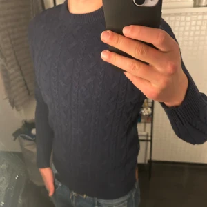 Mörkblå stickad tröja - Kabelstickad mörkblå tröja från 157 med klassisk rund halsringning och ribbade muddar. Tröjan har ett snyggt flätmönster över hela och är långärmad. Använt 1 gång