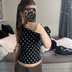 Svart prickig oneshoulder topp med knyt - Säljer en svart oneshoulder topp med vita prickar och snygg knyt-detalj på axeln. Toppen är croppad och har en tight passform som framhäver figuren. Använd 1 gång till fotografering!❤️