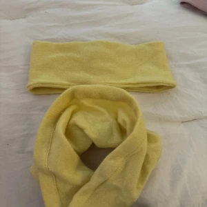 Gul stickad halsduk och pannband - Mysig gul stickad halsduk tillsammans med matchande pannband. Perfekt för att hålla värmen under kyliga dagar. Mjukt material och enkel design som passar till många outfits.