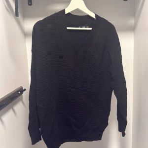 Svart ribbad stickad tröja MNG - Svart stickad tröja från MNG med djup v-ringning och ribbad struktur. Långärmad och i en klassisk, lite loose passform. Perfekt för lager-på-lager och funkar året runt. Snygg till både jeans och kjol.