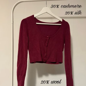 Vinröd croppad kofta i kashmirmix - Supermjuk vinröd croppad kofta med långa ärmar och rund hals. Koftan har knappar framtill och är stickad i en lyxig mix av kashmir, silke och ull. Perfekt för lager-på-lager och ger en snygg siluett till alla outfits.