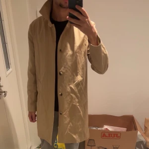 Beige APC rock med knappar - Stilren beige rock med klassisk krage och knäppning framtill. Jackan har raka linjer, två snedställda fickor och är helfodrad. Perfekt för dig som gillar en clean och tidlös look.