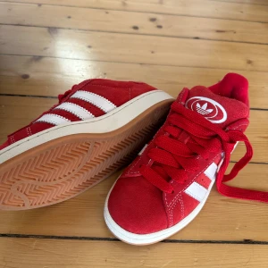 Helt nya! Adidas Campus 00s röda sneakers 37⅓ - Säljer ett par helt nya Adidas Campus 00s sneakers i rött mocka med klassiska vita ränder och logga på plösen. Skorna har platt sula, rund tå och breda röda skosnören. Kommer i originalkartong och har lappar kvar. Helt nya. Aldrig använt. 