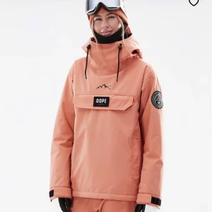 Dope peach vindjacka med huva - Säljer en snygg peachfärgad vindjacka från Dope med stor huva och coola svarta snören. Jackan har en stor ficka framtill med Dope-logga och ett patch på ärmen. Perfekt för dig som gillar streetstyle och outdoor.