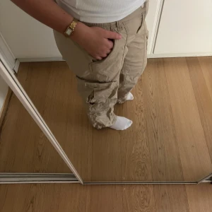 Beiga cargopants med fickor - Säljer ett par beiga cargopants med flera stora fickor på sidorna. Byxorna har en bra passform och är perfekta för en avslappnad streetstyle. Tillverkade i bomull för skön känsla och andningsförmåga.