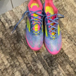 Adidas X Speedportal fotbollsskor - Säljer ett par Adidas X Speedportal fotbollsskor i en riktigt färgstark kombo av blått, neon-gult och rosa. Skorna har snörning, platt sula med fasta dobbar och är tillverkade i syntetmaterial. Perfekta för dig som vill sticka ut på planen!