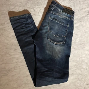 Blå Replay jeans, midwaist, storlek 30/34 - Snygga blå jeans från Replay med slitningar och kontrastsömmar. Klassisk femficksmodell med normal passform och midwaist. Jeansen har en cool tvätt och är perfekta för dig som gillar en avslappnad men stilren look.