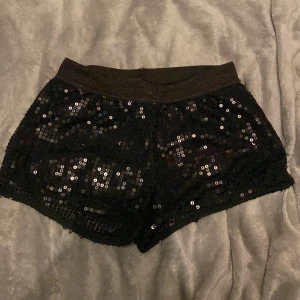 Svarta paljettshorts från KappAhl - Glittriga svarta shorts från KappAhl, täckta med paljetter för extra bling. De har en elastisk midja och skönt material. De är i storlek 146-152