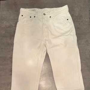 Vita jeansbyxor från Zara - Snygga vita jeansbyxor från Zara med klassisk femficksdesign och raka ben. Byxorna har bälteshällor, knapp och dragkedja framtill samt en stilren look som passar till många outfits. Tillverkade i bomull för en skön känsla.